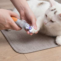 CozyPaws™ LED pet nail clipper in use — owner trimming relaxed white cat's nails with LED light illuminating the quick, orange non-slip grip handle, cat lying calmly on grey mat on wooden floor - Image 2