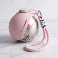 CozyPaws™ pink dog water bottle close-up — soft silicone panel folded over stainless steel sphere body with bow ribbon print detail, carabiner carry loop and pink braided wrist strap on white marble surface - Image 6